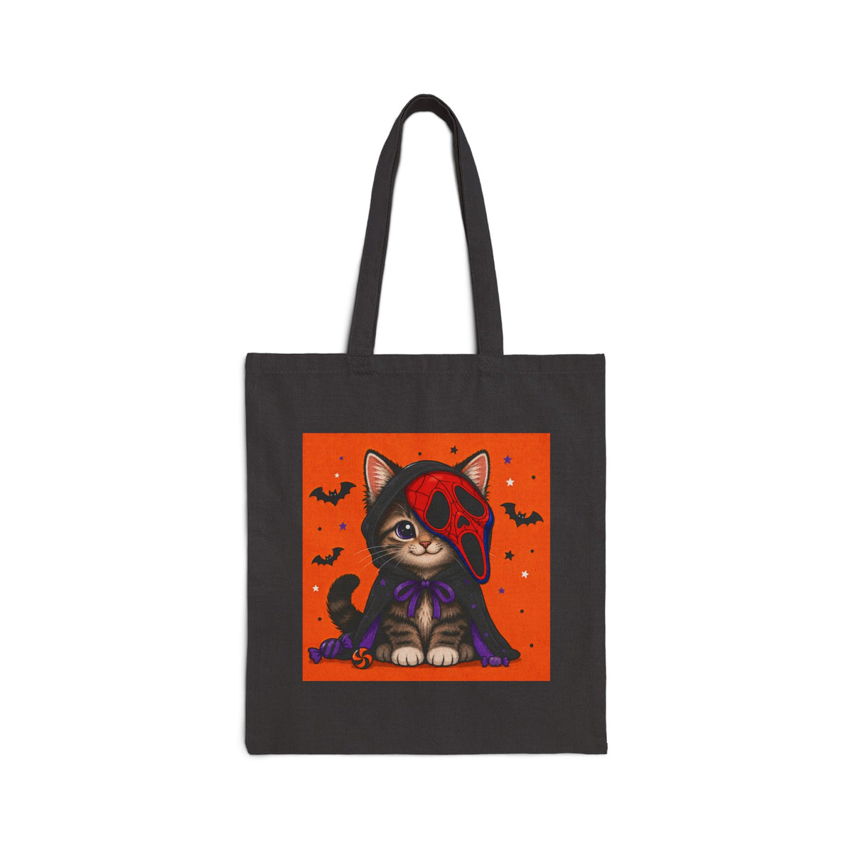 A black canvas tote bag with long handles, featuring a square graphic print of a cute cartoon cat dressed in a red Ghostface mask and purple cape against an orange background with bats and stars.
