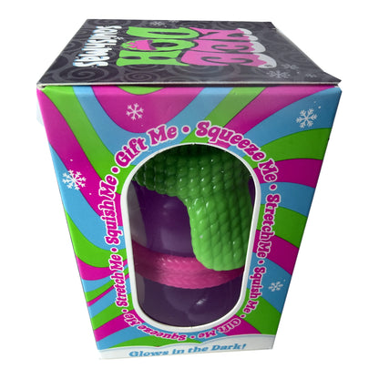 A boxed novelty toy labeled 'Squishy Me' with a visible green textured squishy ball inside a colorful retail box. The box has pink, blue, and green striped sides, a black top panel, and text including 'Gift Me • Squeeze Me' and 'Glows in the Dark!'.