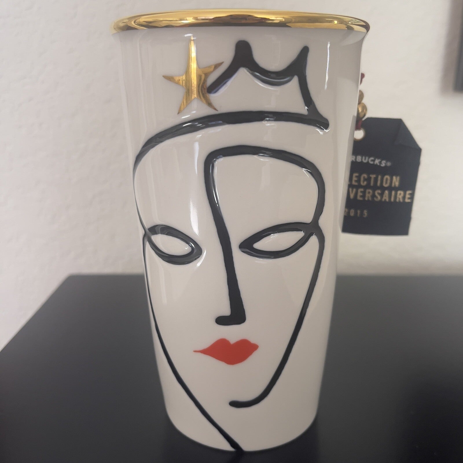 White tumbler with a face design and gold rim on a black surface.