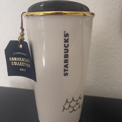 Starbucks tumbler with gold rim and black lid, featuring the brand name and 'Anniversary Collection' tag.