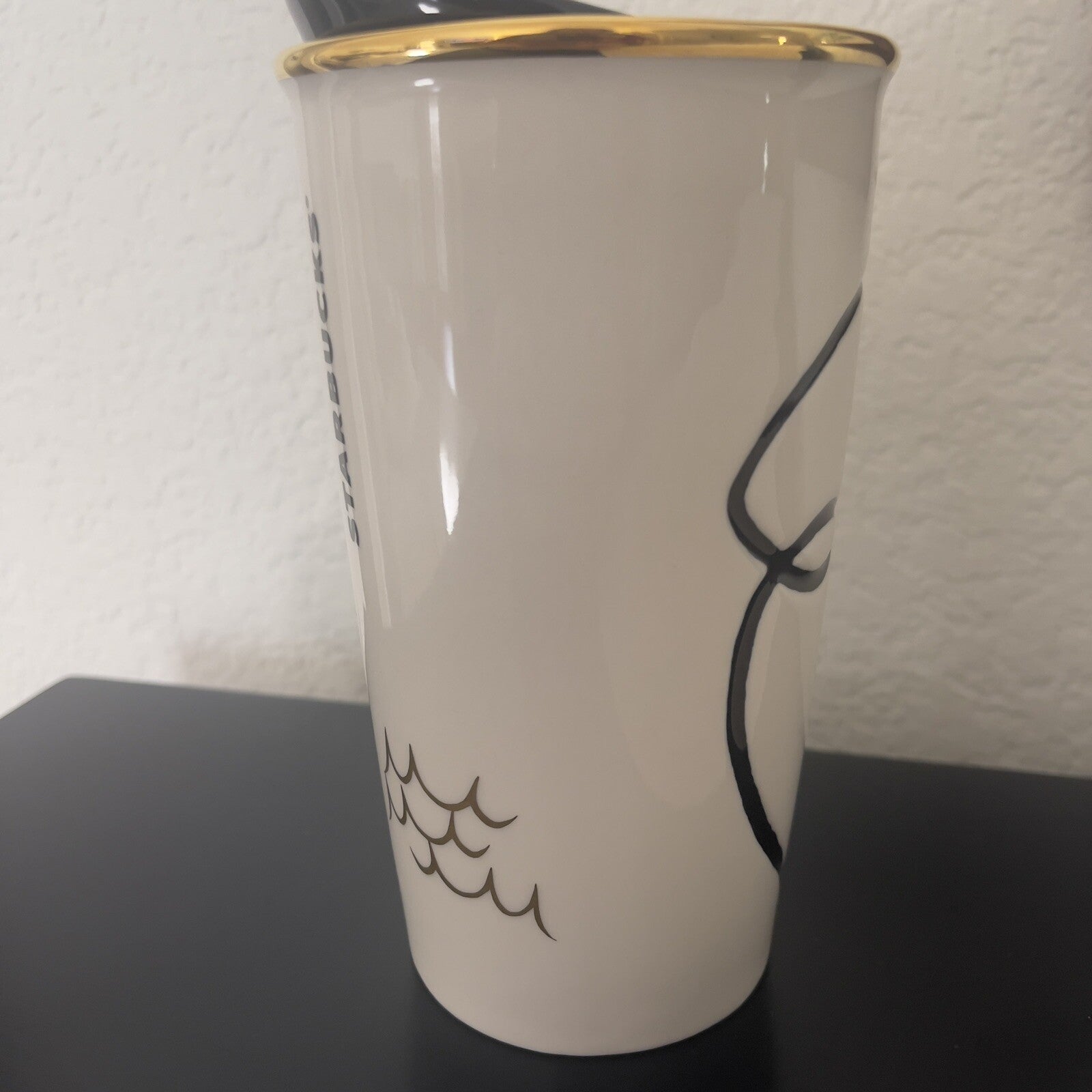 White mug with black wave design and gold rim on a dark surface.