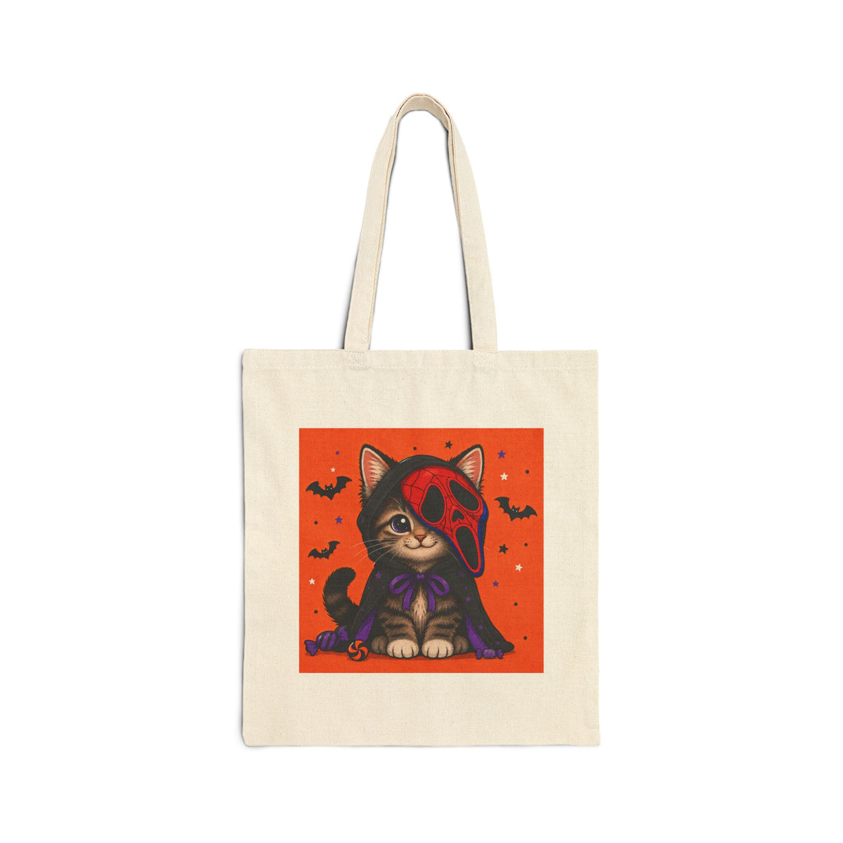 An off-white canvas tote bag with a square graphic print of a cute cartoon kitten wearing a red skull mask and purple cape against an orange background, shown on a plain white studio background.