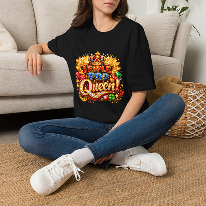 A woman sitting cross-legged on a woven rug in front of a beige sofa, wearing a black graphic T-shirt with a colorful 'Triple Pop Queen' design, blue jeans, and white sneakers.