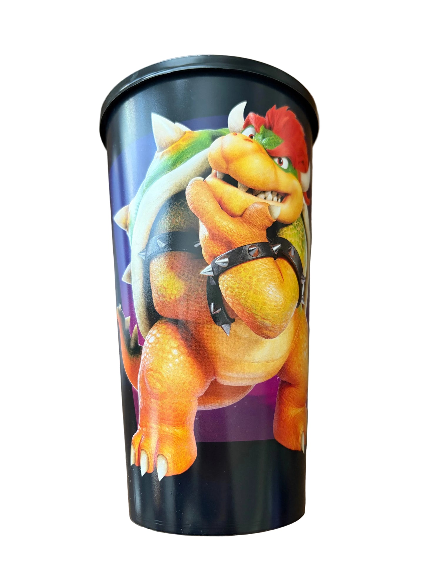 A cylindrical travel tumbler featuring a printed graphic of Bowser from the Super Mario franchise, resting on a brown wooden surface.
