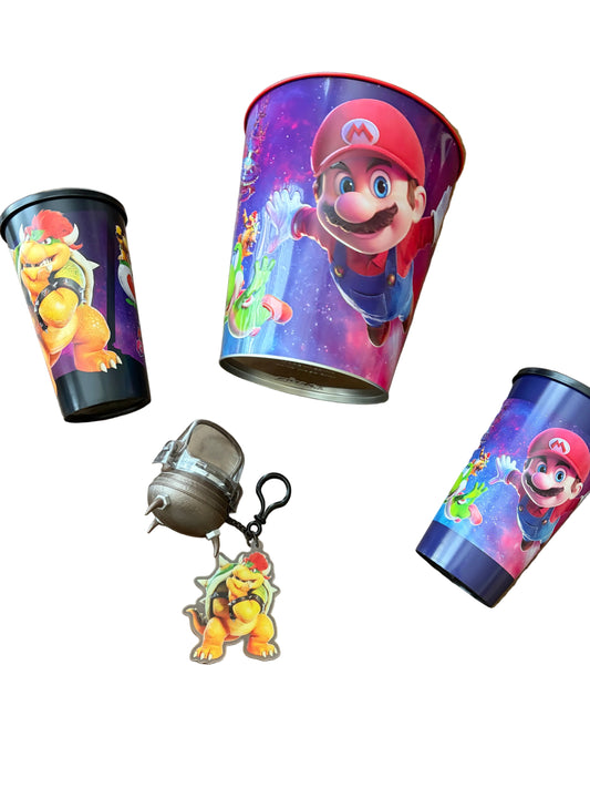 Three printed metal tins with colorful Mario-themed artwork and a small metallic keychain lying on a wooden surface.