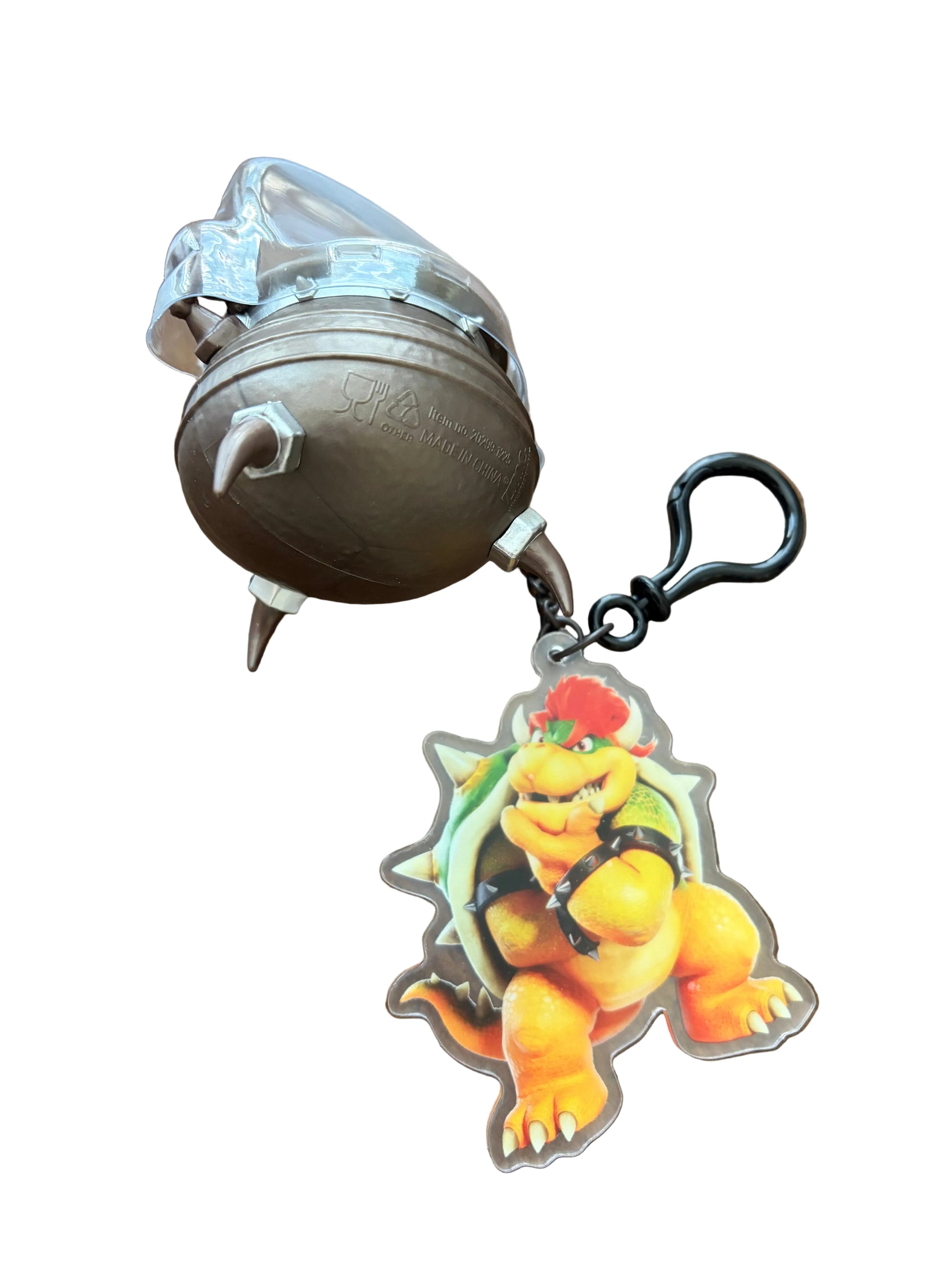 A Bowser-themed keychain featuring a metallic bronze ball with a small keyhole protruding from it, alongside a clear acrylic charm of Bowser on a green shell, attached to a black metal clip, displayed on a wooden surface.