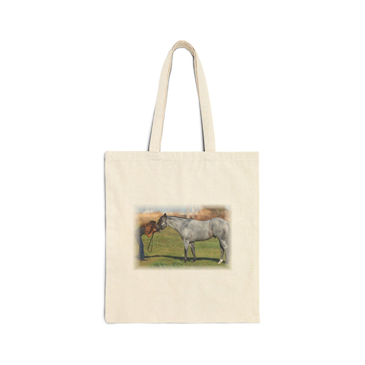 An off-white canvas tote bag with two handles, featuring a printed illustration of a gray horse standing in a grassy field on the front.