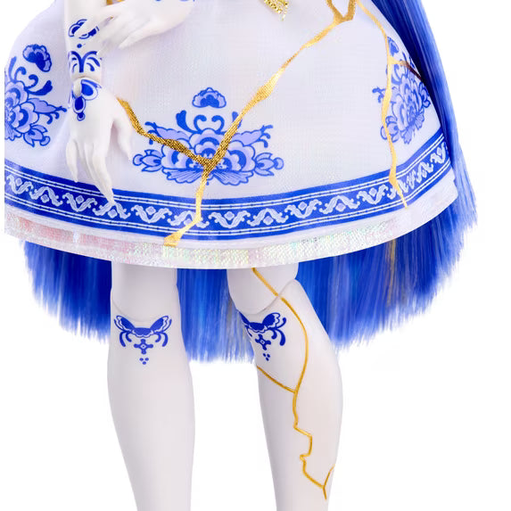 Close-up of a doll or fashion figure wearing a white dress with blue floral patterns, blue fringe, and gold decorative lines, paired with white tights featuring blue motifs.