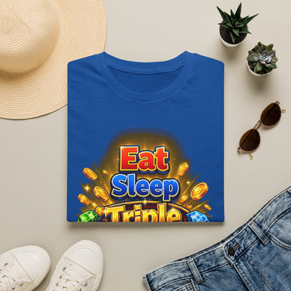 A folded blue T-shirt with a colorful 'Eat Sleep Triple' graphic print, styled in a flat lay with a straw hat, white sneakers, denim shorts, sunglasses, and small potted succulents on a light beige background.