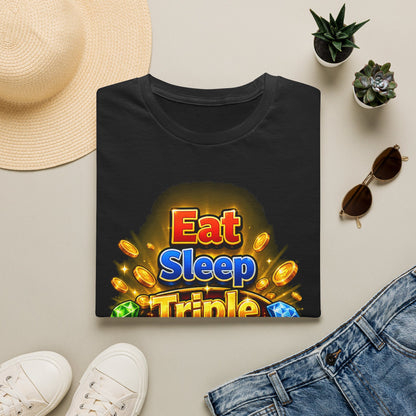 A folded black T-shirt with a colorful 'Eat Sleep Triple' graphic print, styled in a flat lay with a straw hat, white sneakers, blue jeans, sunglasses, and small potted succulents on a light beige background.