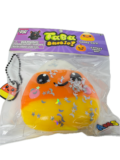 A packaged squishy toy shaped like a crescent moon with a black cat face, decorated with silver glitter stars and a pink crescent moon. The toy is sealed in a clear plastic bag with a purple 'Treats Squeezies' branded card insert.