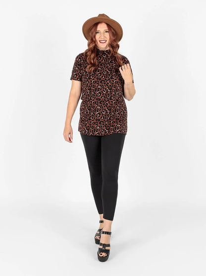 Woman wearing a leopard print top and black leggings on a white background