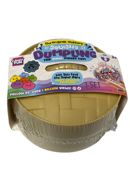A packaged 'Dumpyling' squishy toy from Crafty Creations, shown in its clear plastic wrap with a colorful cardboard header card. The product is a round, beige-colored squishy with a grid pattern, and the packaging features various colorful graphics and text.