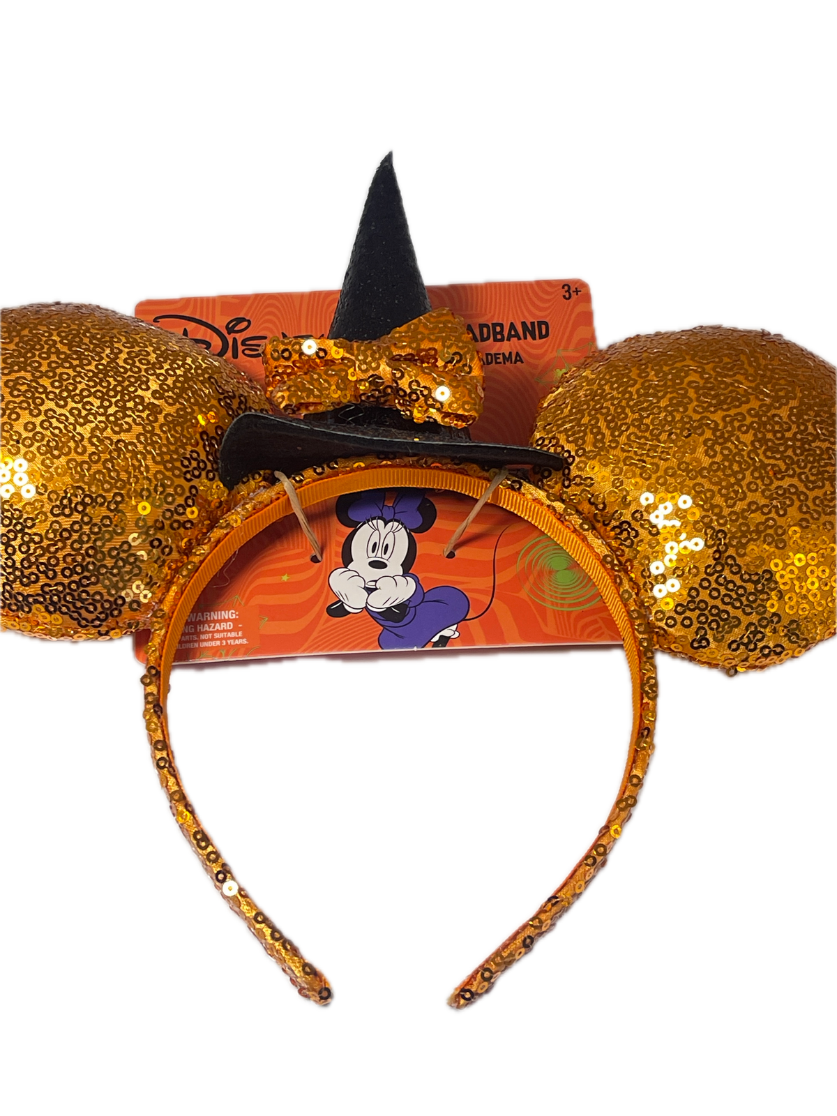 A gold sequined Mickey Mouse ears headband with a black witch hat and matching bow, displayed in front of its orange Disney packaging on a white background.