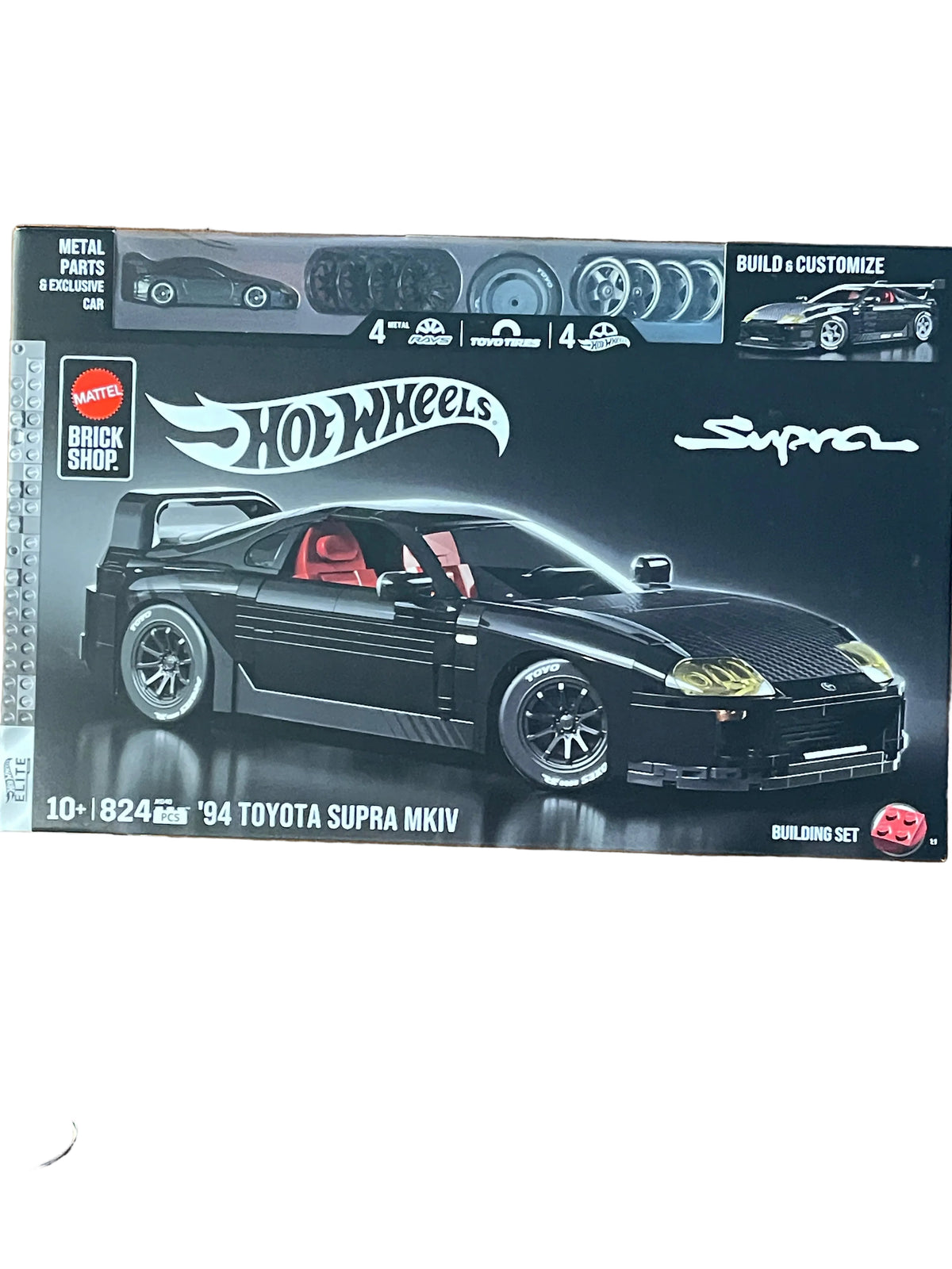 Hot Wheels Brick Shop '94 Toyota Supra MK IV building set box on a wooden floor, showing a black sports car model with red interior and toy parts icons at the top.