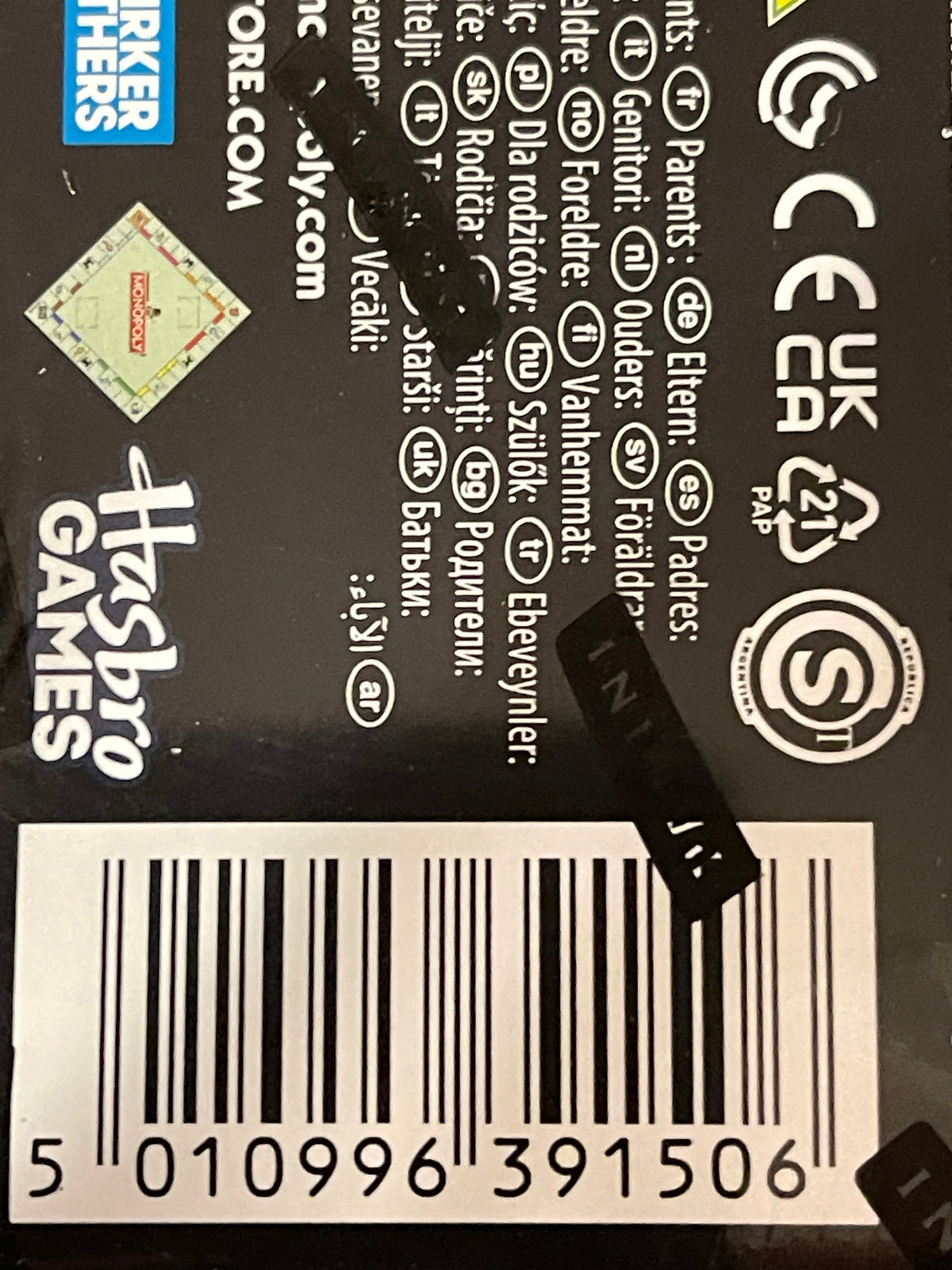 Close-up of the back of a Hasbro Games product box showing product information text, barcodes, certification marks, and a black retail tag attached near the center.