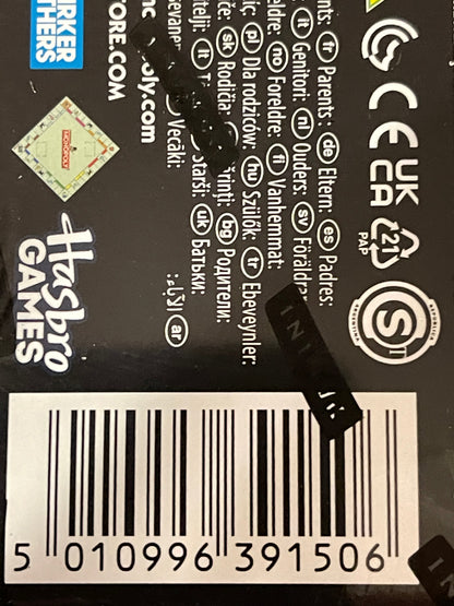 Close-up of the back of a Hasbro Games product box showing product information text, barcodes, certification marks, and a black retail tag attached near the center.