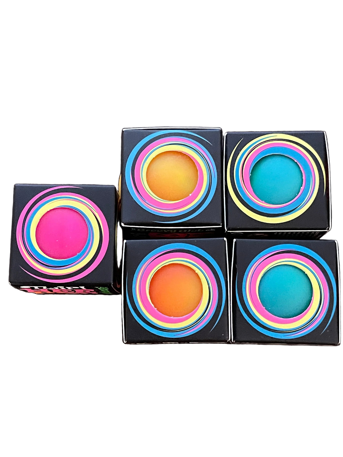 Four square black cosmetic boxes arranged on a dark wooden surface, each featuring a colorful concentric ring design in pink, yellow, blue, and green around a bright circular center. One box is open, showing a pink product inside.