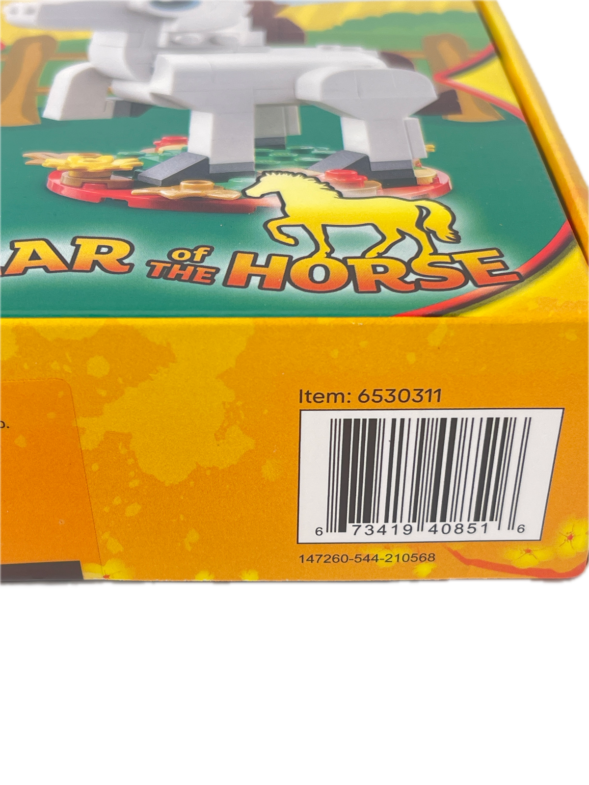 Close-up of a toy box corner showing a yellow side panel with a barcode and part of a green front illustration featuring the text 'AR OF THE HORSE' and a horse graphic.
