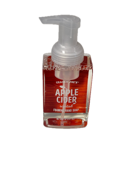 A bottle of Trader Joe's Apple Cider scented foam hand soap, showing the clear pump dispenser and red liquid inside a clear bottle with a red label, isolated on a white background.