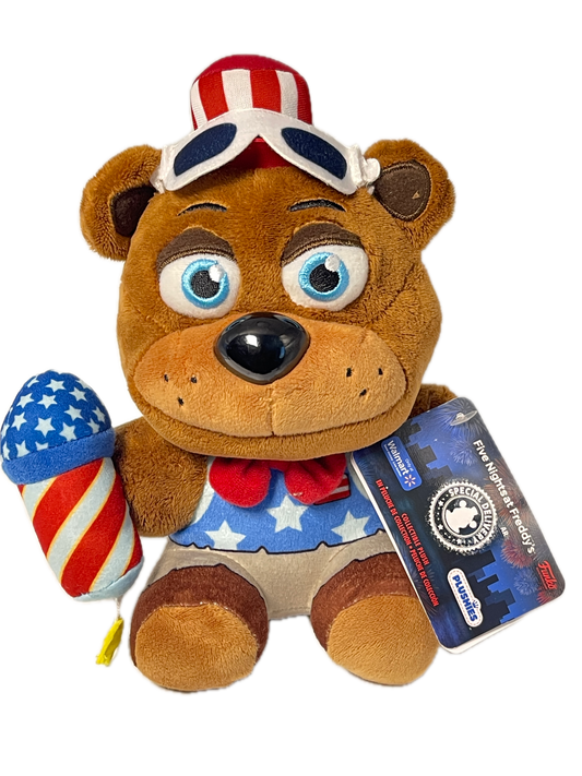 A plush teddy bear toy with a patriotic American flag theme, featuring a red, white, and blue star-spangled body, a matching star-spangled hat, and a blue hangtag that reads 'Five Biggest Freddy's' and 'PUSHINS'.