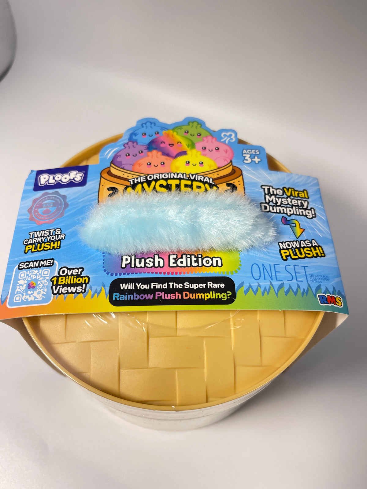 A packaged toy product labeled 'Plush Edition' with a pastel blue fuzzy plush item resting on top of a yellow basket-weave style base inside a round container. The front packaging has colorful graphics and text including 'The Original Viral Mystery Plush,' 'Twist & Cramwhim Plush,' and 'Plush Edition.