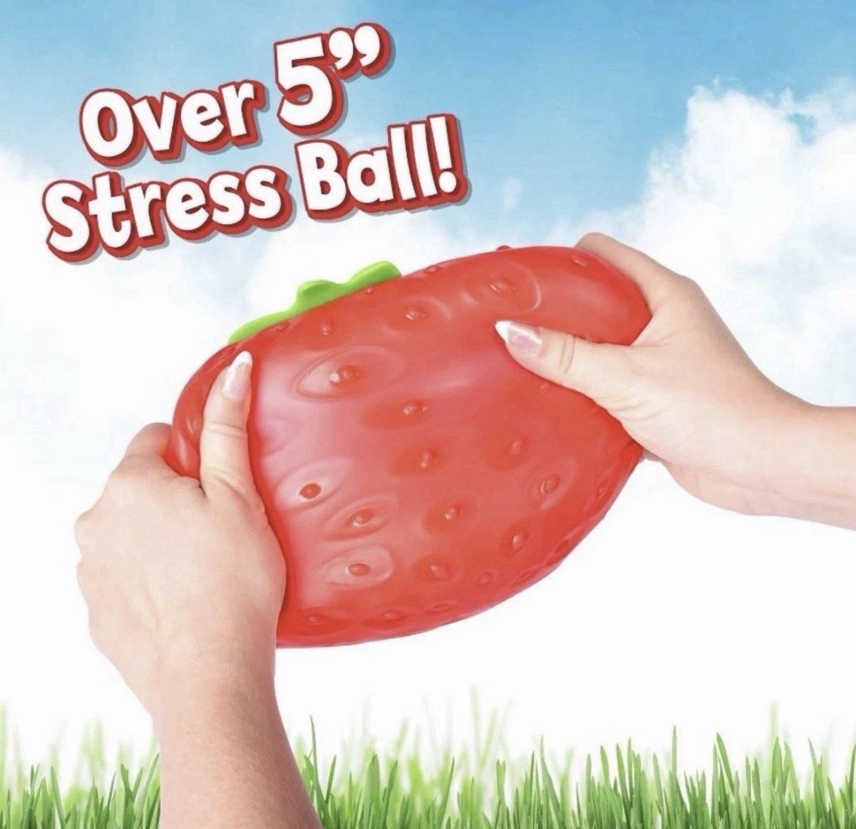 Strawberry-shaped stress ball held by hands with a sky and grass background
