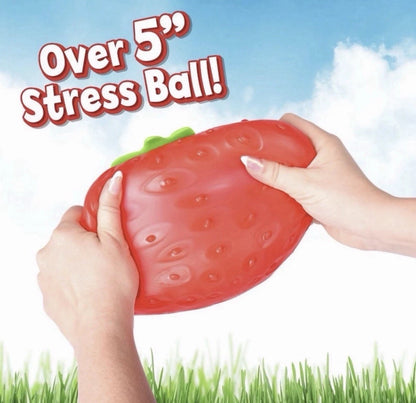 Strawberry-shaped stress ball held by hands with a sky and grass background