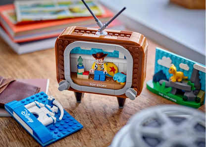LEGO set with a vintage TV displaying scenes from 'Toy Story' on a wooden surface.