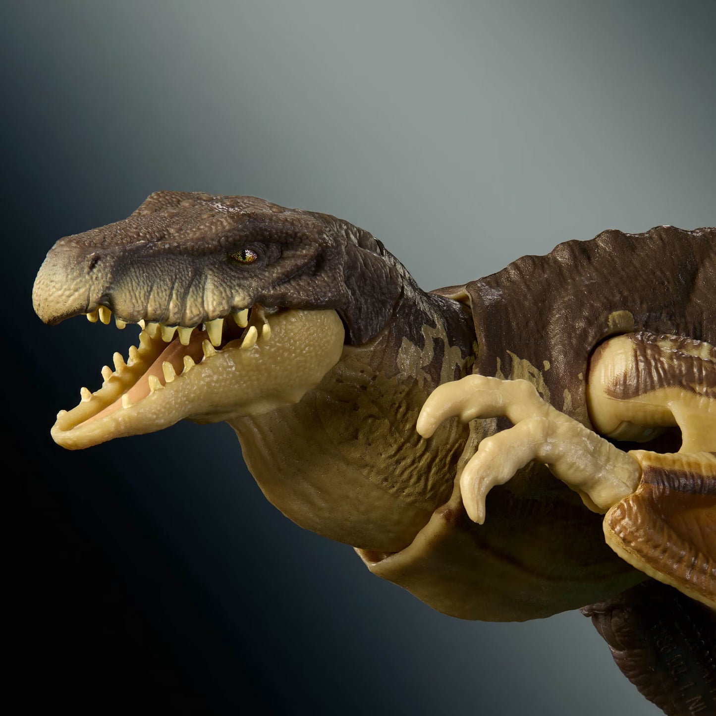 A close-up of a detailed dinosaur toy or figurine with an open mouth showing sharp teeth, textured brown and tan skin, and pale yellow claws, set against a dark gradient background.