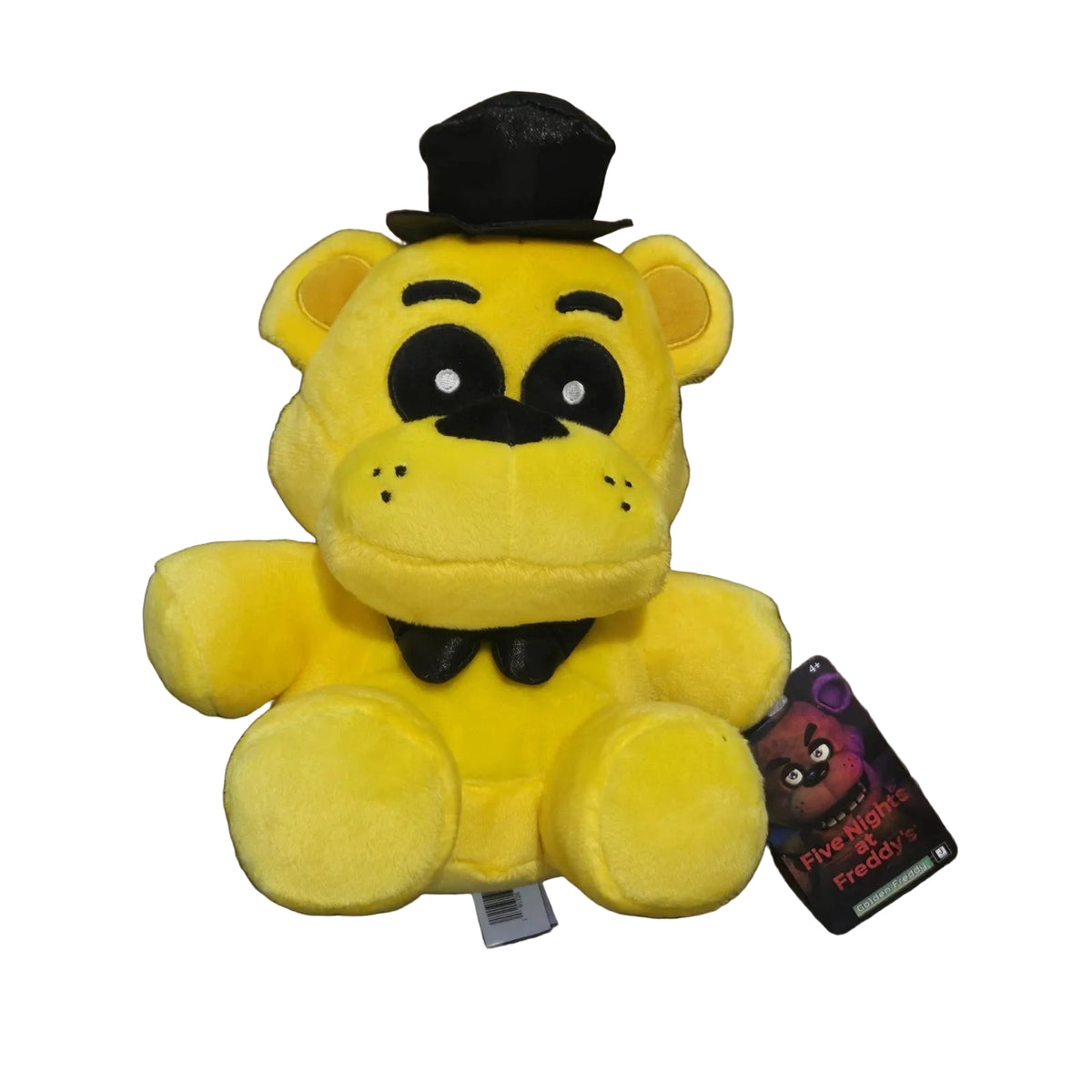 A yellow plush toy bear wearing a black top hat and black bow tie, photographed on a dark wood floor. A hangtag for 'Five Nights: Freddy's' is attached to the right side.