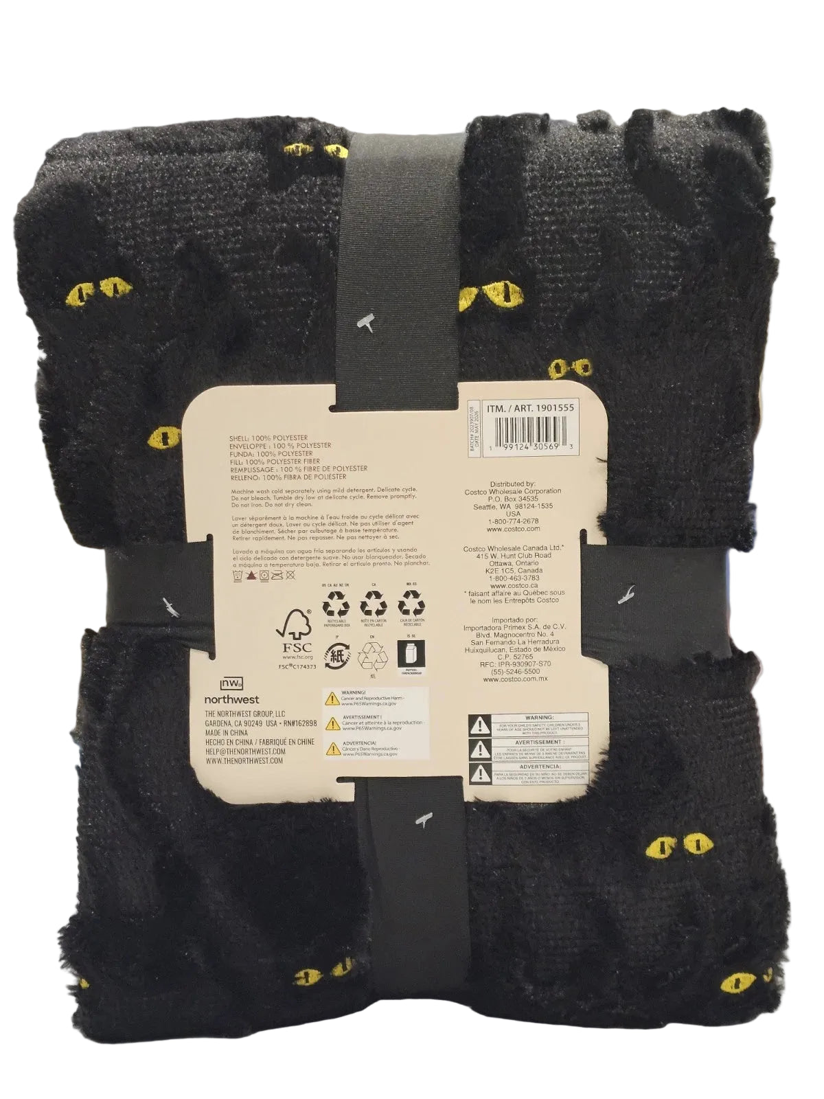 A folded black plush throw blanket with small yellow cat-eye patterns, wrapped in a dark strap with a product information label attached, photographed indoors against a blurred background.